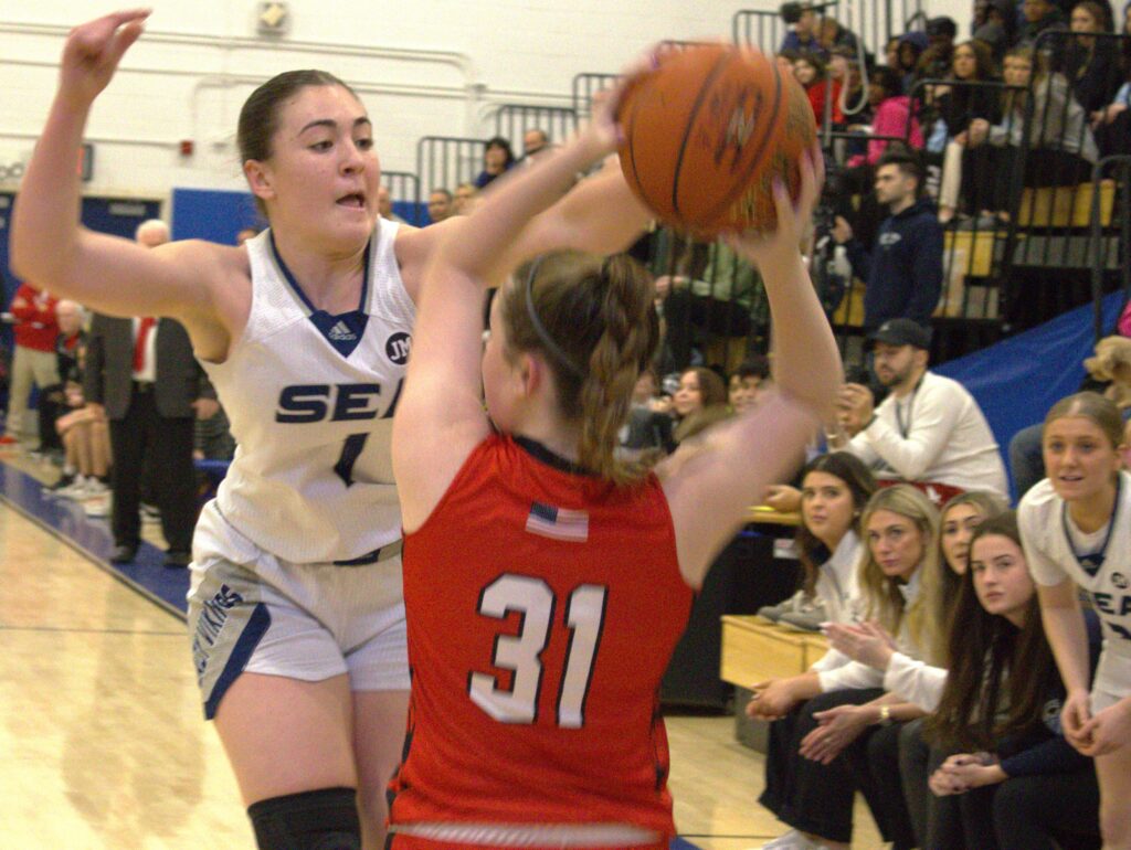 A girl is participating in a basketball tournament and trying to block a shot.