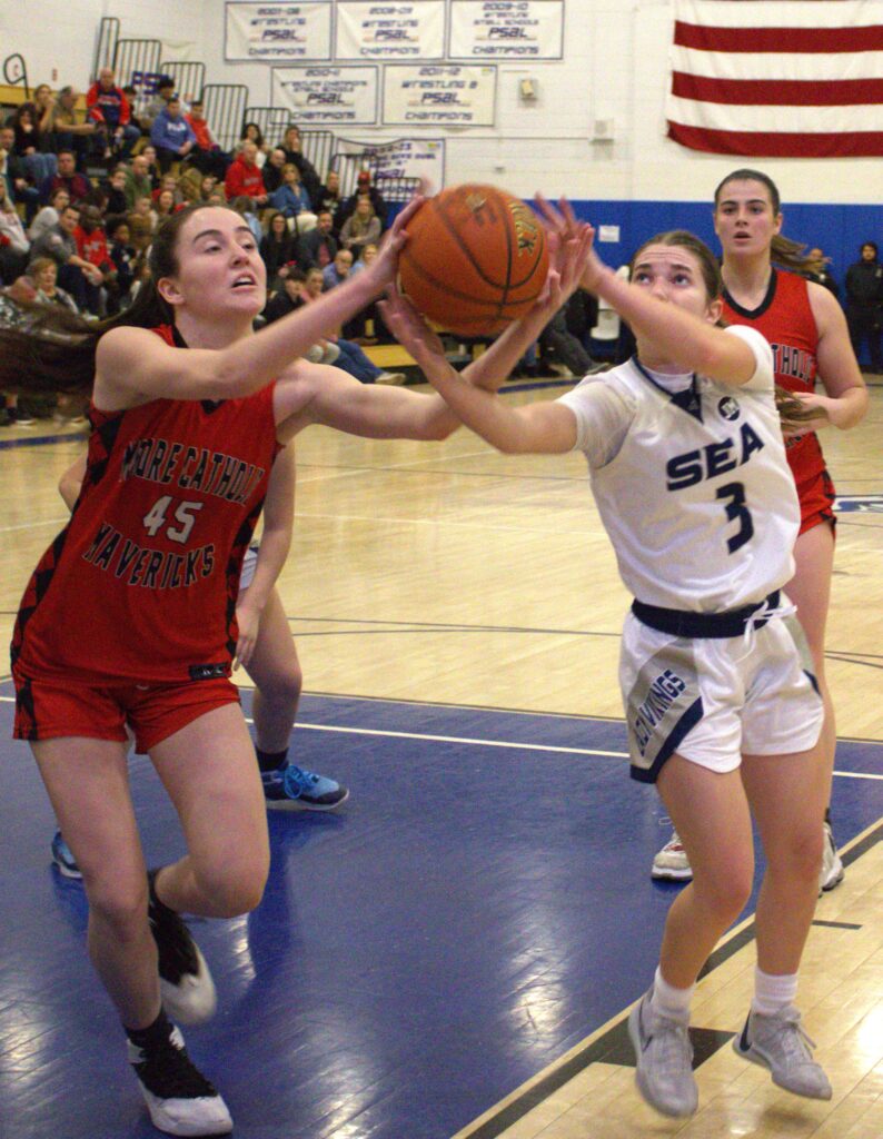 At a high school basketball game, a girl stands determined at the hill, with the sea in her view, as she tries to block a shot.