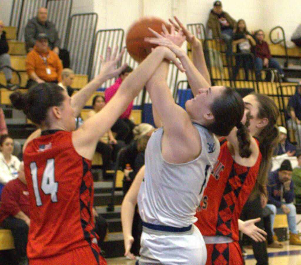 A girl is participating in a basketball tournament and attempting to block a player's shot while standing on a hill near the sea.