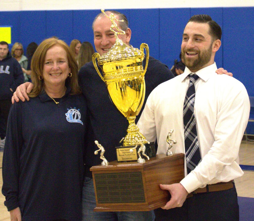 A group of people posing with the Borough President's Cup Tournament trophy by the sea.