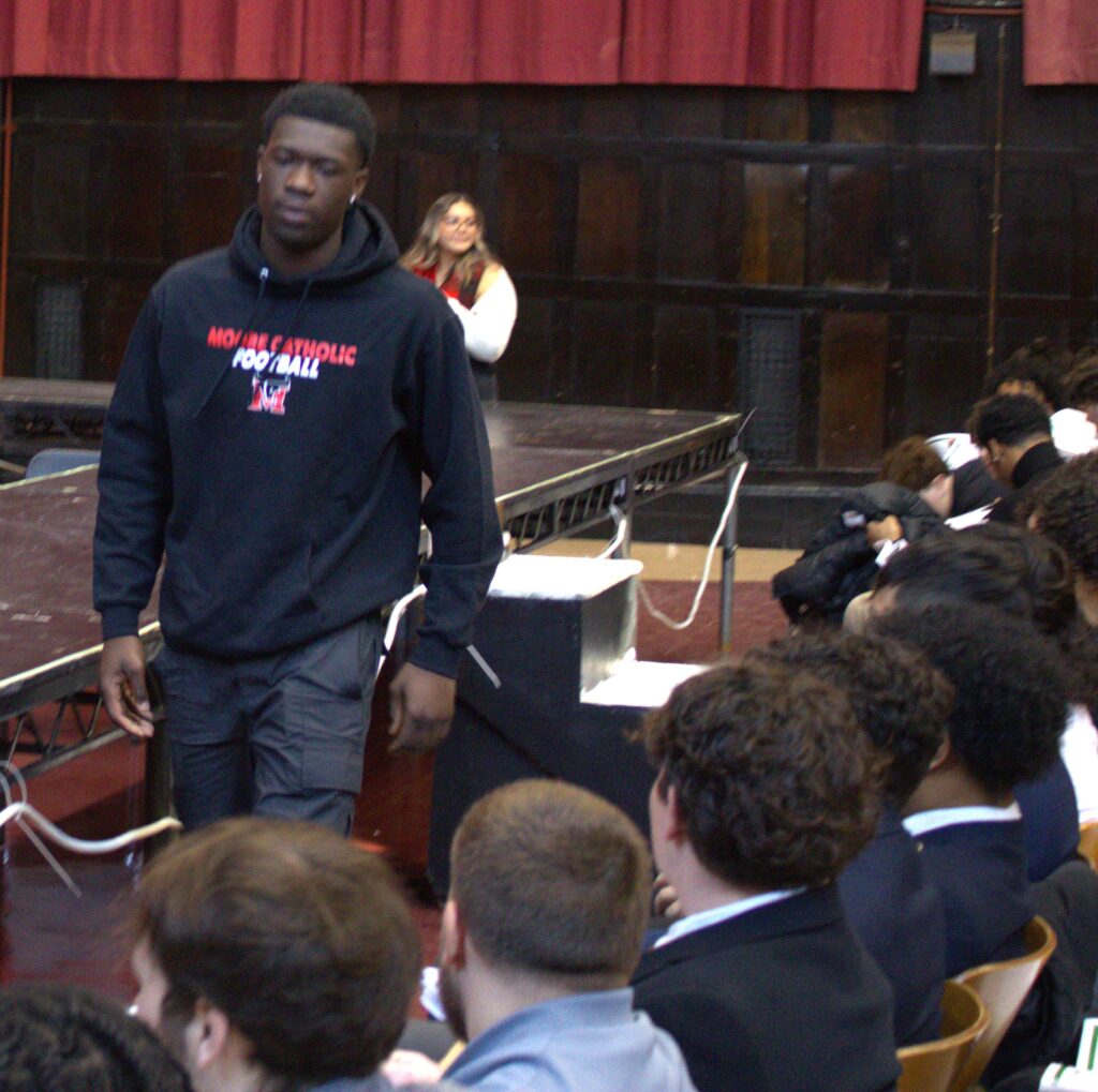 A man in a black hoodie standing in front of a group of people at an awards ceremony.