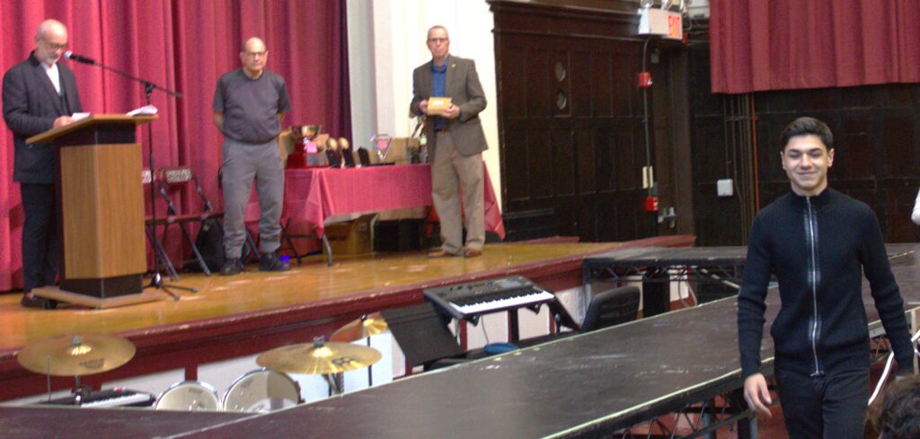 A man standing on a stage accepting an award in front of a group of people.