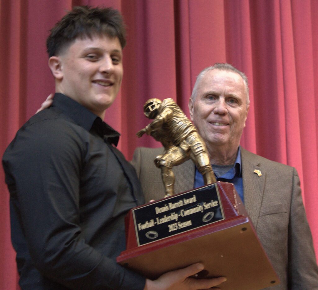 A man named Smith holding a trophy in front of a curtain.