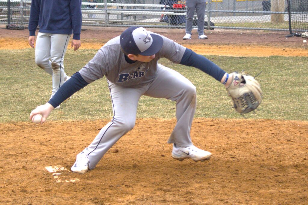 A baseball player at St. Joseph's University is bending down to catch a ball on the field.