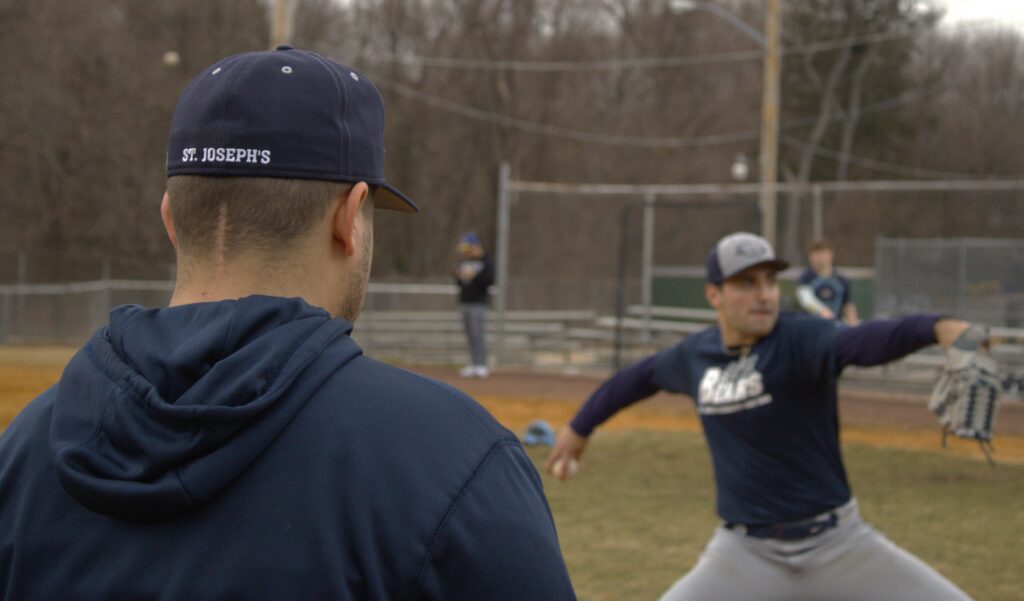 A baseball player is throwing a ball on a field at St. Joseph's University.