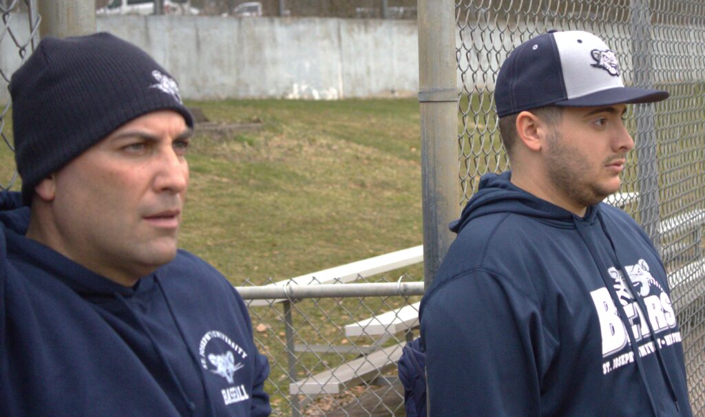 Two men standing next to each other on a baseball field at St. Joseph's University.