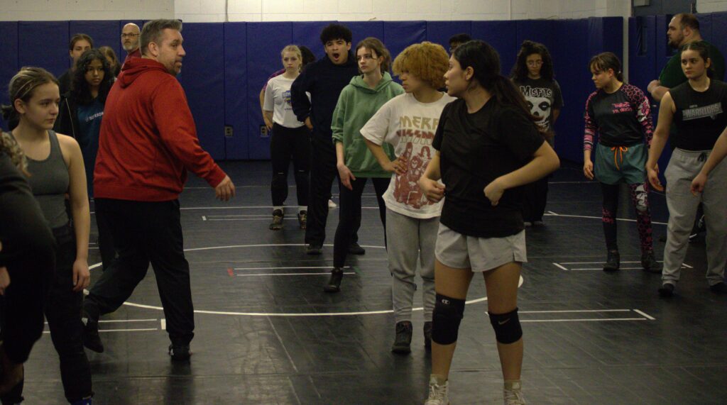 A group of PSAL island girls' wrestlers in a gym.